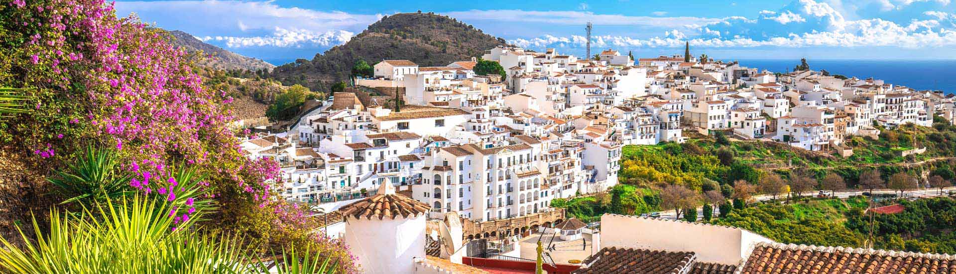 Żywiołowa panorama malowniczego miasteczka na wybrzeżu, białe domy z czerwonymi dachami, otoczone bujną zielenią, z widokiem na góry i ocean, idealna do inwestycji w nieruchomości turystyczne.